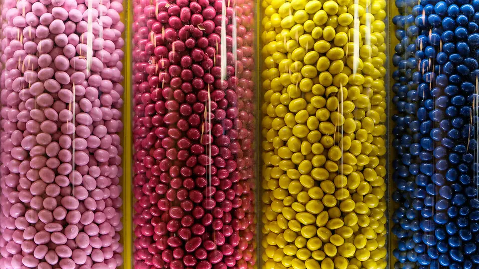 Gläser mit Zuckerperlen in Rosa, Gelb und Blau nebeneinander