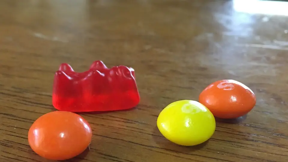 Ein rotes Fruchtgummi und drei Kaubonbons auf einem Holztisch
